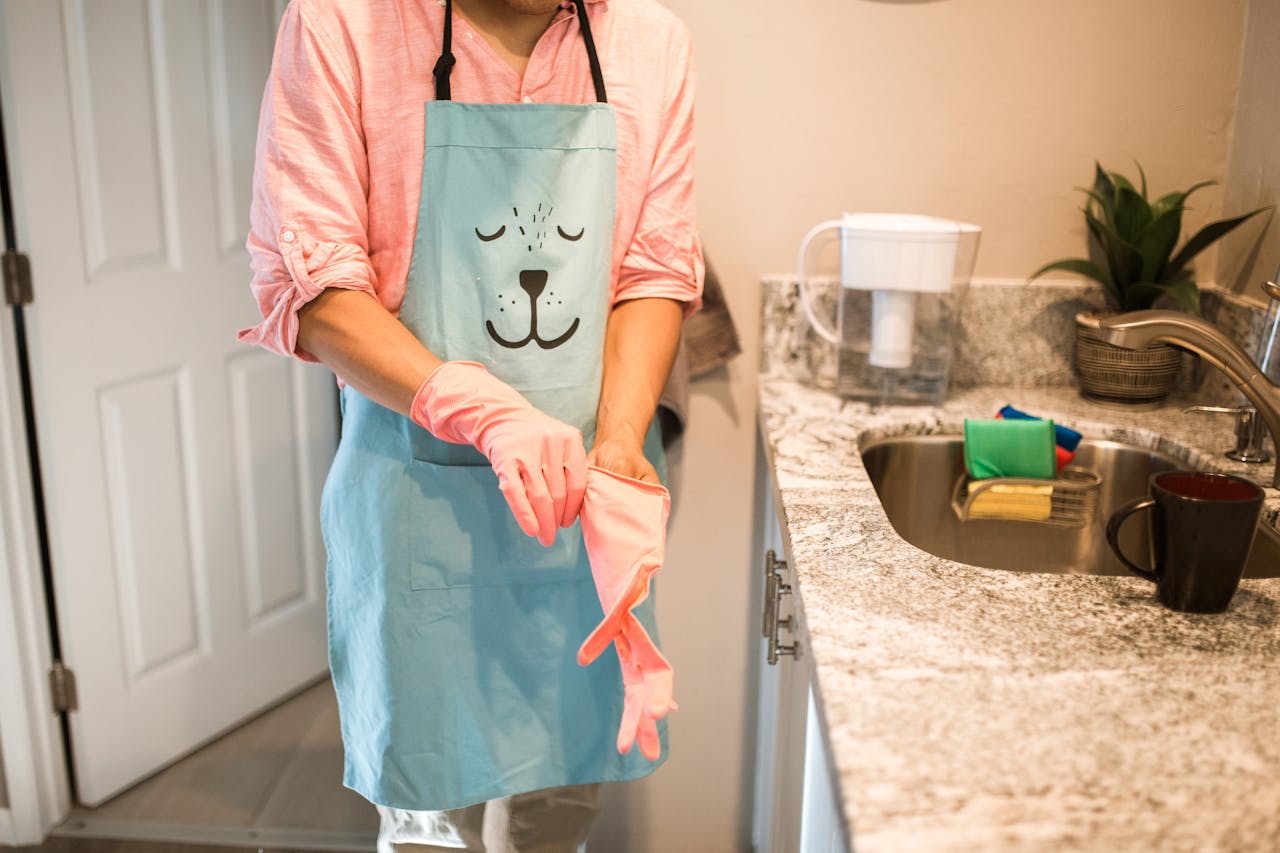 Person in a kitchen putting on rubber gloves with a cute animal-themed apron. Indoor setting.
